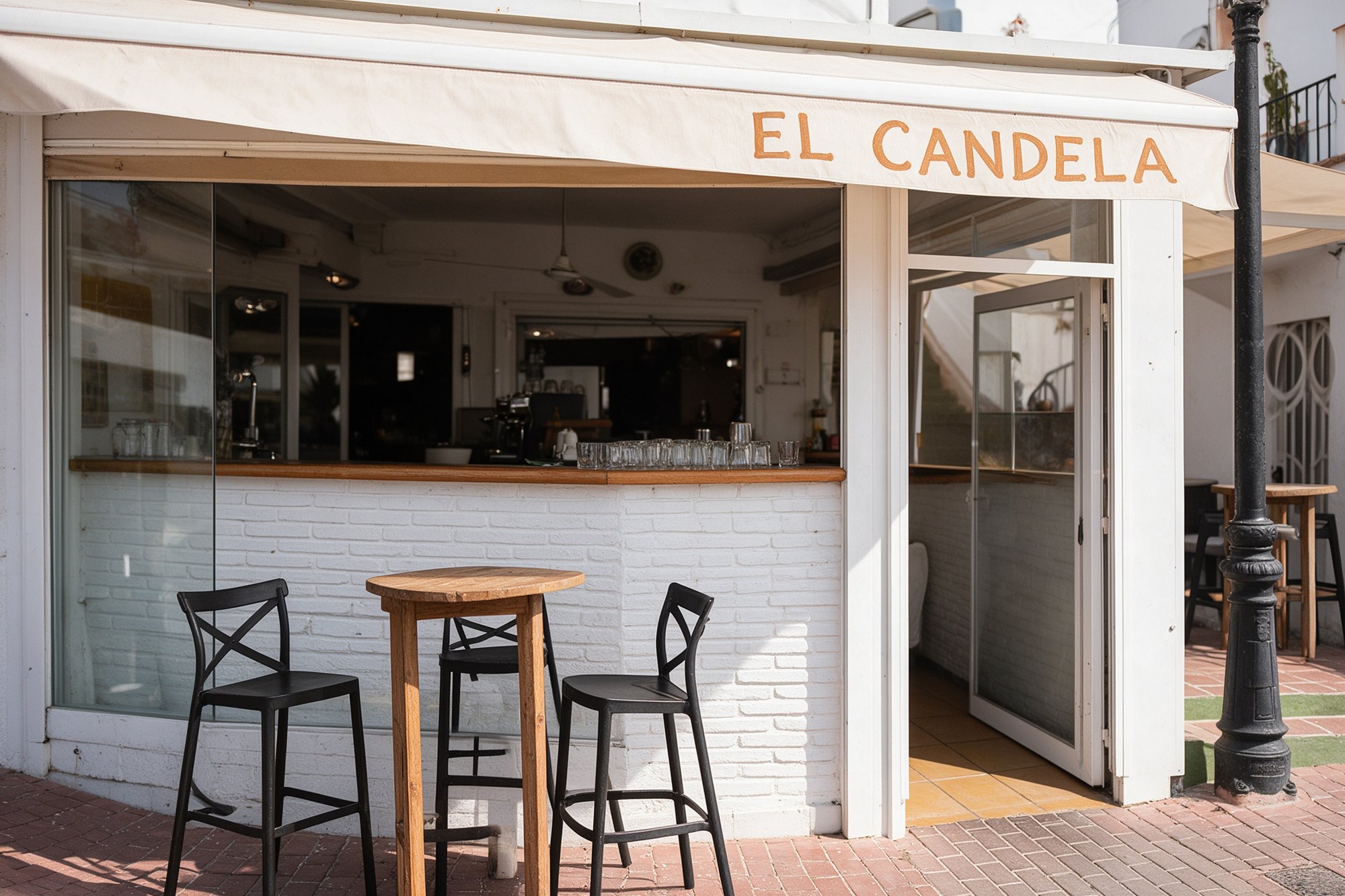Barra de tasca vista a través del escaparate abierto, mueble de ladrillo blanco encalado y taburetes altos junto a la acera